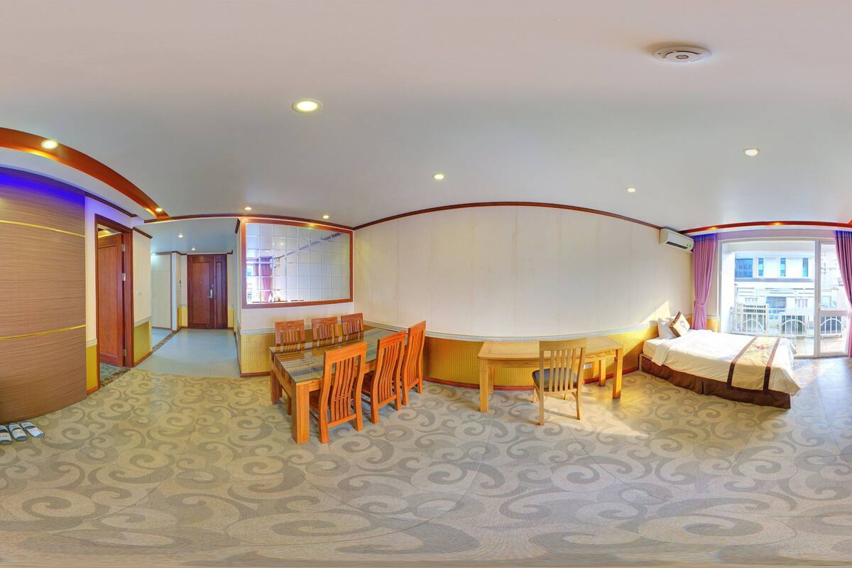 Una habitación de hotel moderna con una pared de madera curvada, una zona de comedor con sillas y una mesa, y una cama con vistas al exterior.