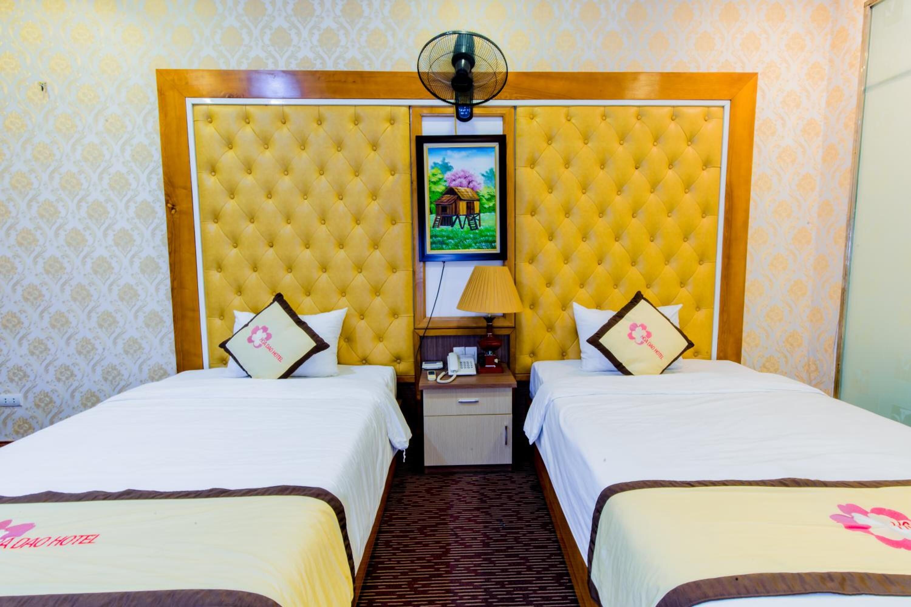 A hotel room with two beds, a tufted headboard, a small bedside table with a lamp, and a framed picture on the headboard.