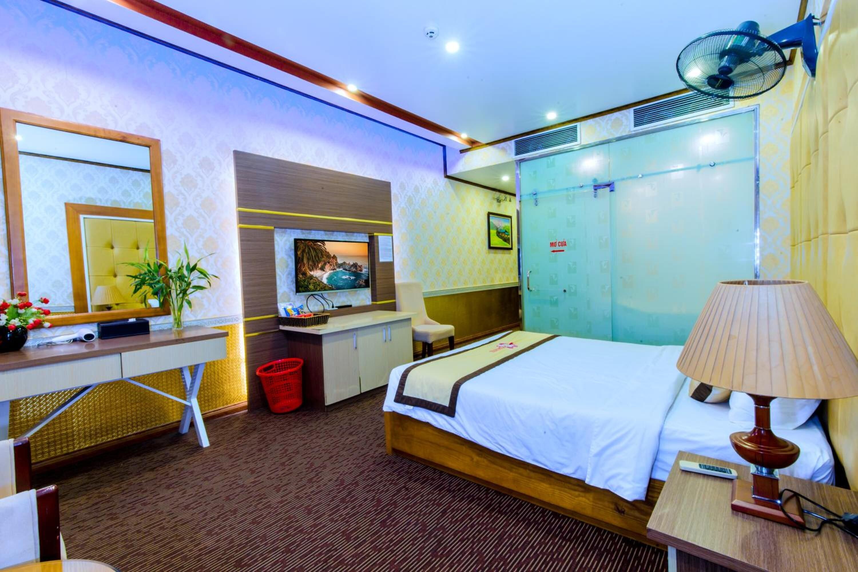 Ein Hotelzimmer mit Bett, Schreibtisch, Stuhl, Fernseher und Ventilator.