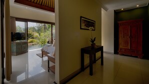 Una habitación amplia con un gran ventanal, techo de madera, una mesita con una planta y un aparador tradicional.