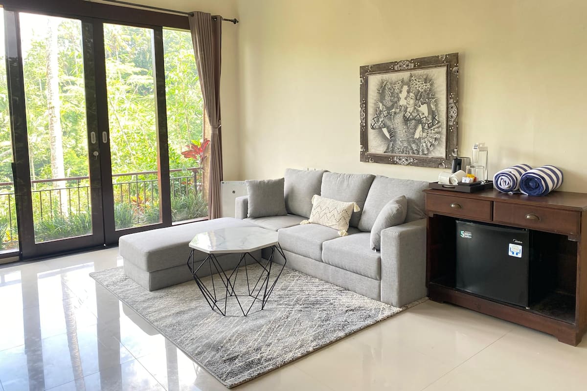 A modern living room with a grey sofa, a coffee table, a small side table, a framed artwork, and a minibar.