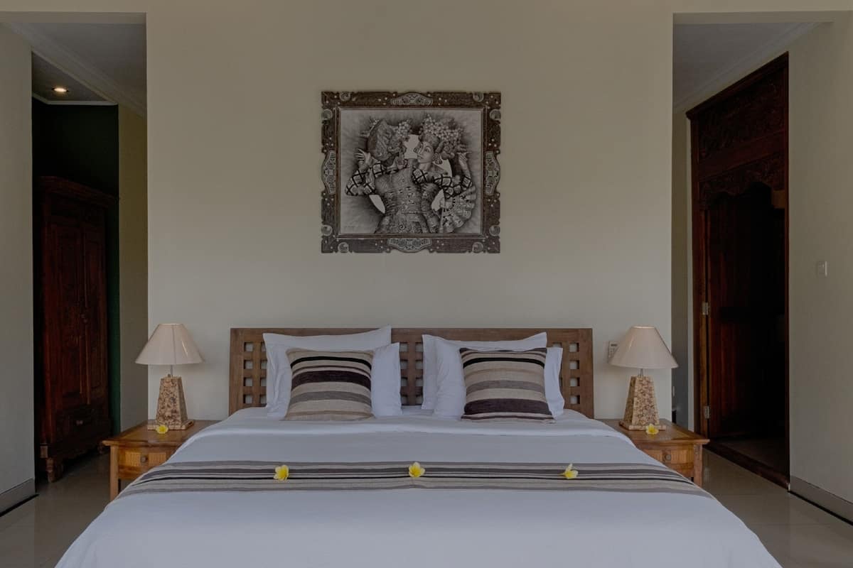 A bedroom with a wooden bed, two bedside tables, a wall-mounted picture, and a door on the right.