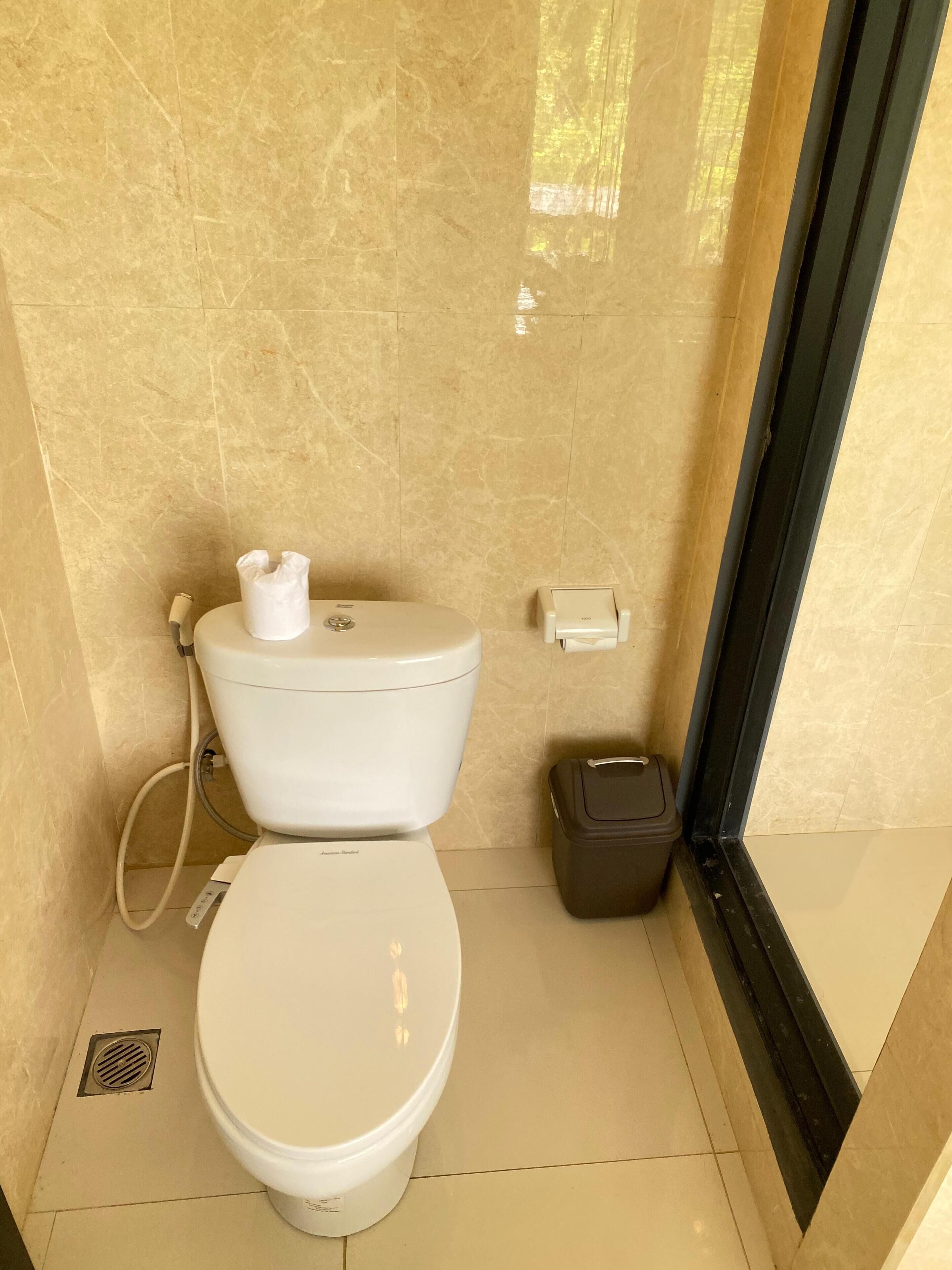 A small, clean bathroom with a toilet, a trash bin, and a hand dryer.