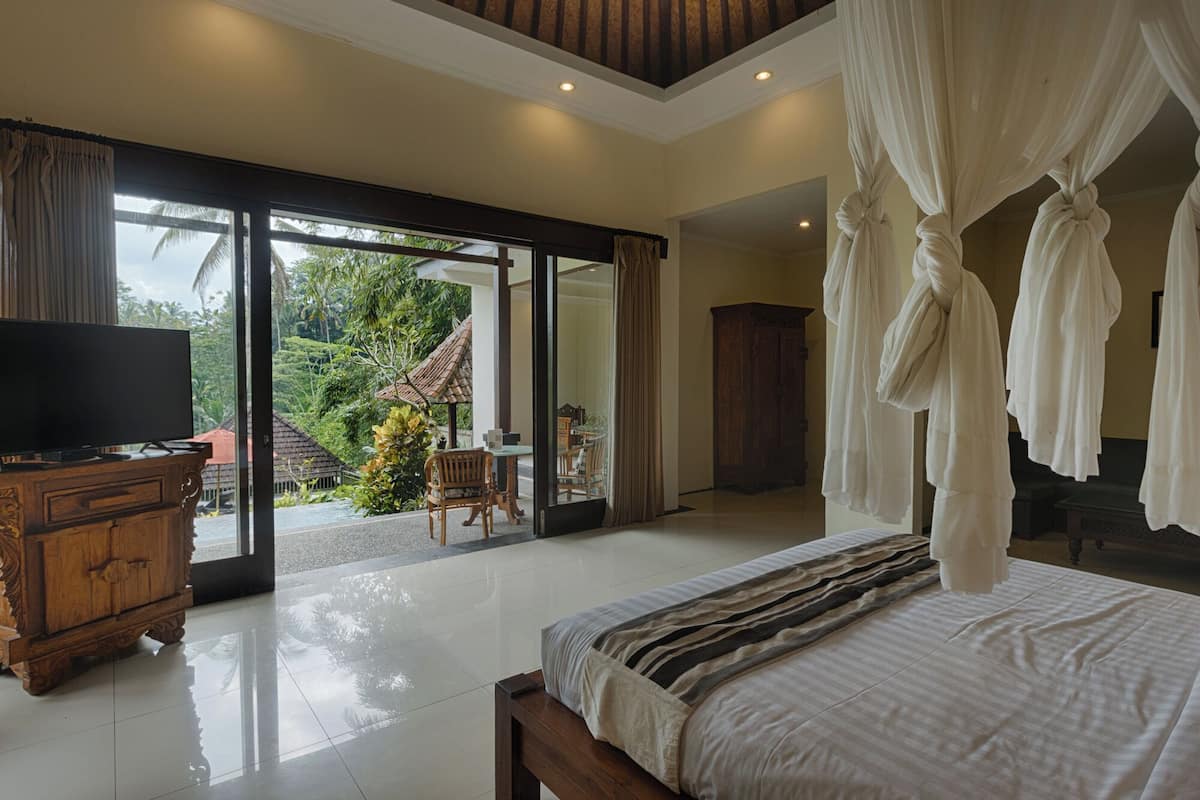 A bedroom with a large bed, a television, and a view of a garden through a sliding door.