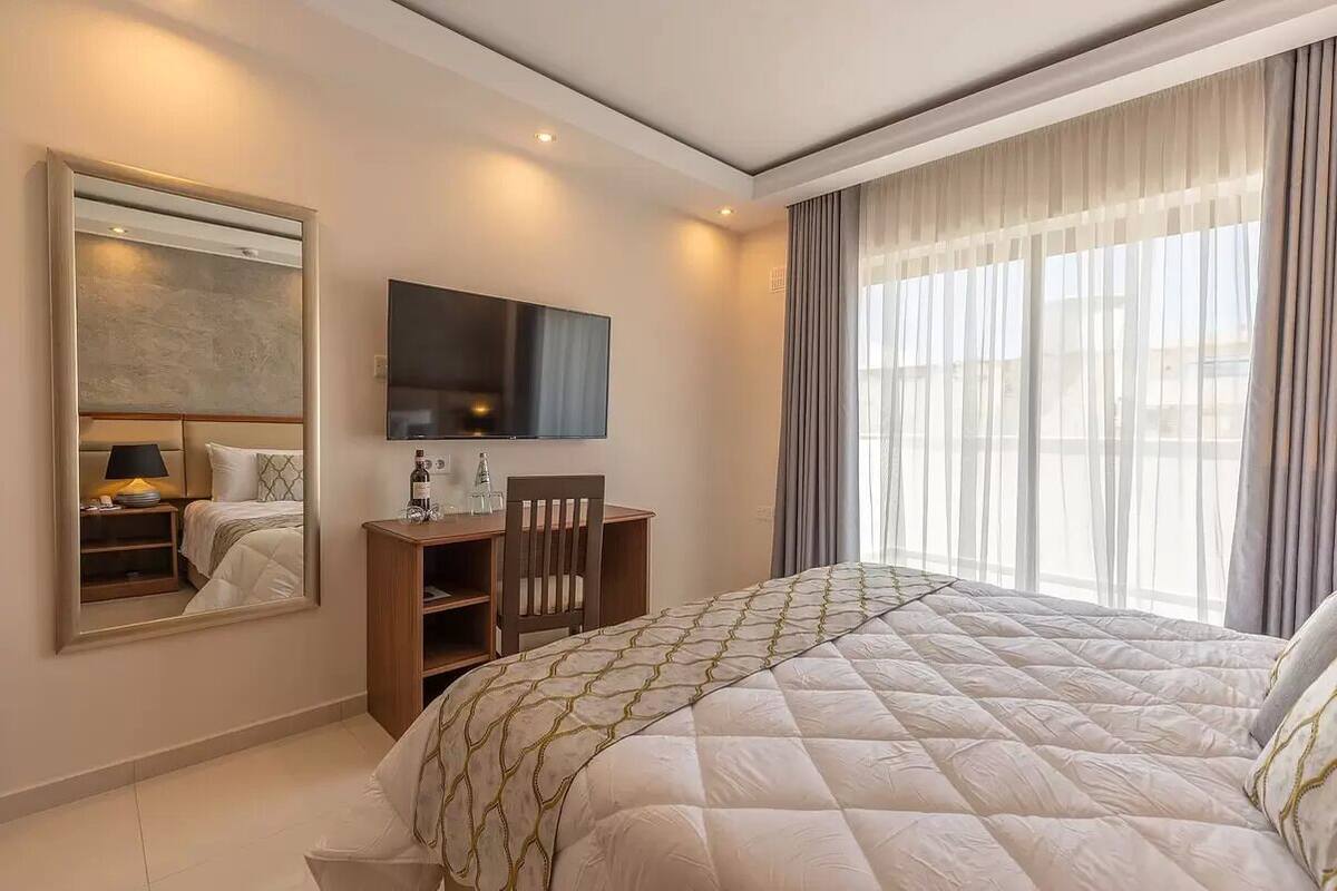 Ein modernes Hotelzimmer mit einem großen Bett, einem Schreibtisch, einem Fernseher und einem großen Fenster mit Vorhängen.
