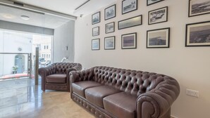 A spacious lobby with a brown leather sofa and armchairs, a glass door leading outside, and a wall adorned with framed black and white photographs. - Dun Gorg Guest House (Marsaxlokk)