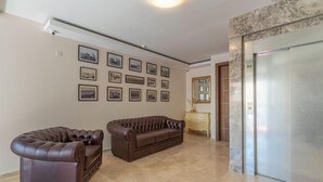 A spacious lobby with a brown leather sofa, a smaller armchair, and a marble floor. There are framed pictures on the wall and an elevator to the right. - Dun Gorg Guest House (Marsaxlokk)