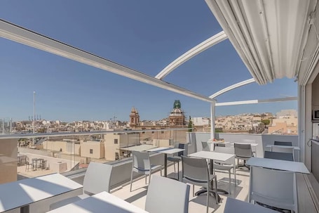 A rooftop terrace with tables and chairs, offering a view of a cityscape including a prominent dome and buildings.