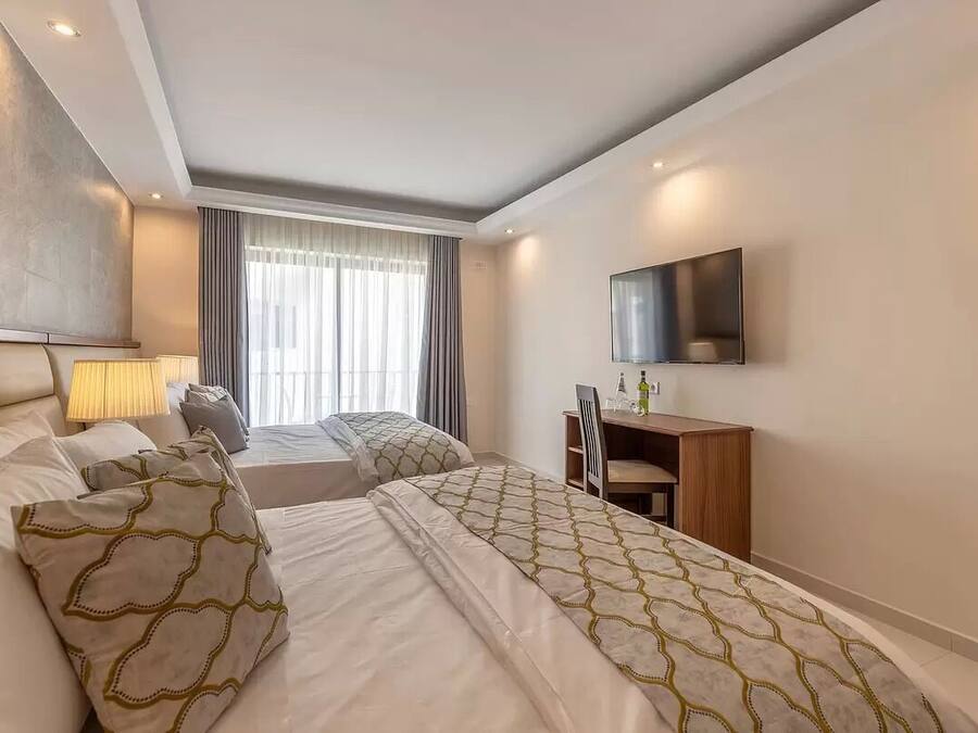 A hotel room with two beds, a desk, a chair, a TV, and a window with curtains.