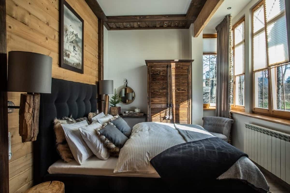 Een slaapkamer met een groot bed, houten wanden, een raam met jaloezieën en een spiegel aan de muur.