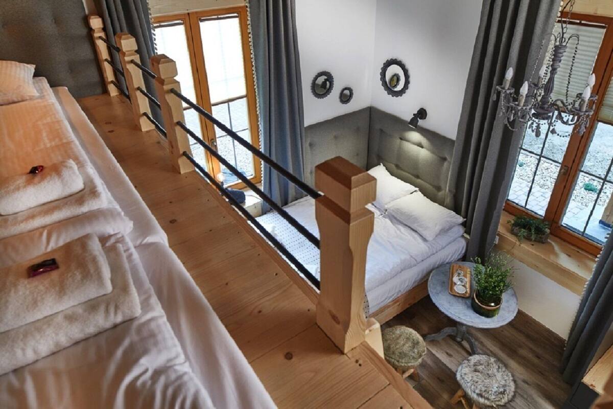 Een kamer met een bed, een klein krukje, een ronde tafel met een plant, en een kroonluchter.
