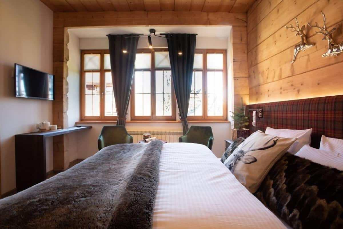 Een gezellige kamer met een groot bed, een televisie, een houten hoofdbord en een raam met gordijnen.