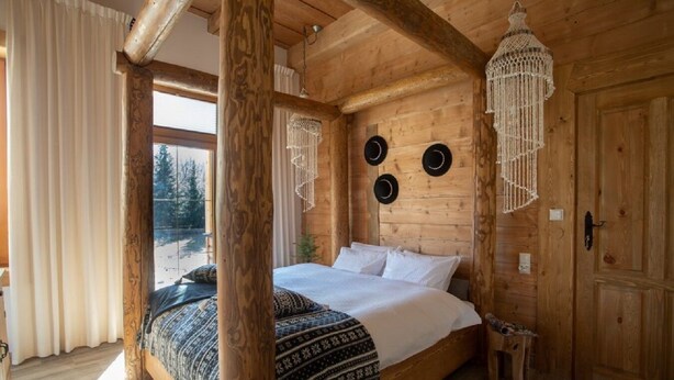 Une chambre aménagée dans une cabane en bois, avec un grand lit, un luminaire suspendu et une vue sur l’extérieur.