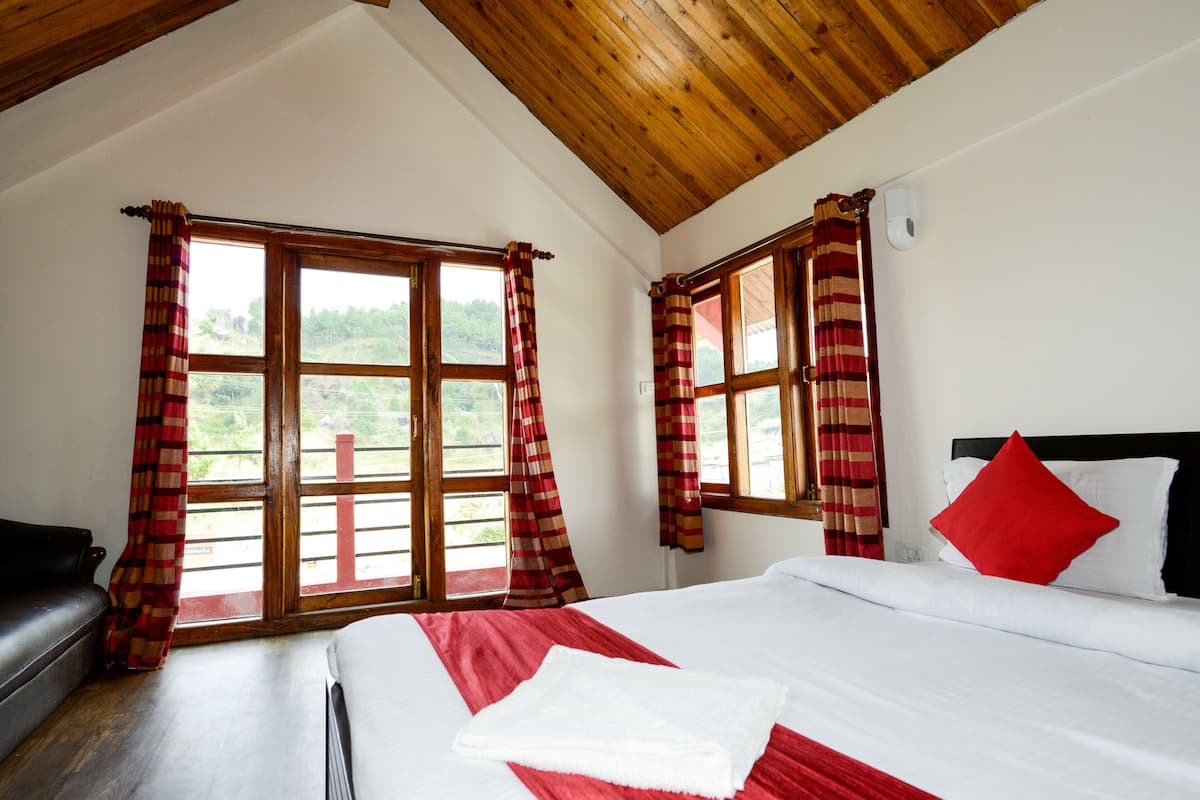 A bedroom with a bed, a bench, and large windows with curtains.