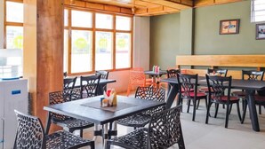 A restaurant with multiple tables and chairs, large windows, and a wooden ceiling.