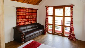 A room with a wooden ceiling, a dark brown leather sofa, a wooden floor, and a window with red curtains.