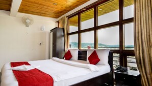A hotel room with a large bed, a desk with a telephone, and a view of the outdoors through large windows.