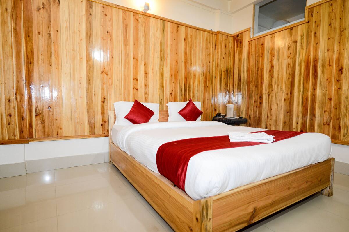 A wooden-framed bed with white bedding and red pillows in a room with wooden panel walls.