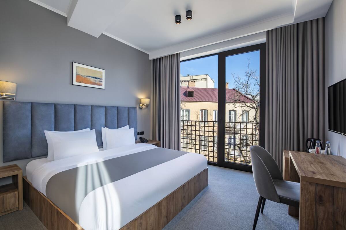Habitación de hotel moderna con una cama grande, un escritorio y vistas de la ciudad a través de amplios ventanales.