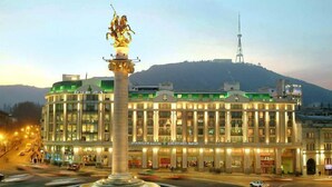 A hotel with a central fountain, multiple floors, and a view of a hill with a tower in the background. - BARNOVI BOUTIQUE HOTEL (Tbilisi)