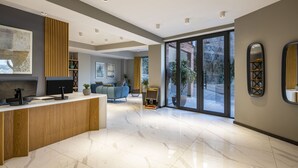 A modern reception area with a wooden counter, a large painting, and a seating area with a sofa and chairs. - BARNOVI BOUTIQUE HOTEL (Tbilisi)