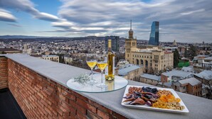 A balcony with a glass table, a bottle of wine, and a plate of nuts and dried fruits. - BARNOVI BOUTIQUE HOTEL (Tbilisi)