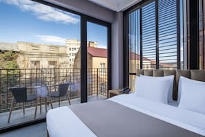 A modern hotel room with a large bed, a view of the city, and a balcony with chairs. - BARNOVI BOUTIQUE HOTEL (Tbilisi)
