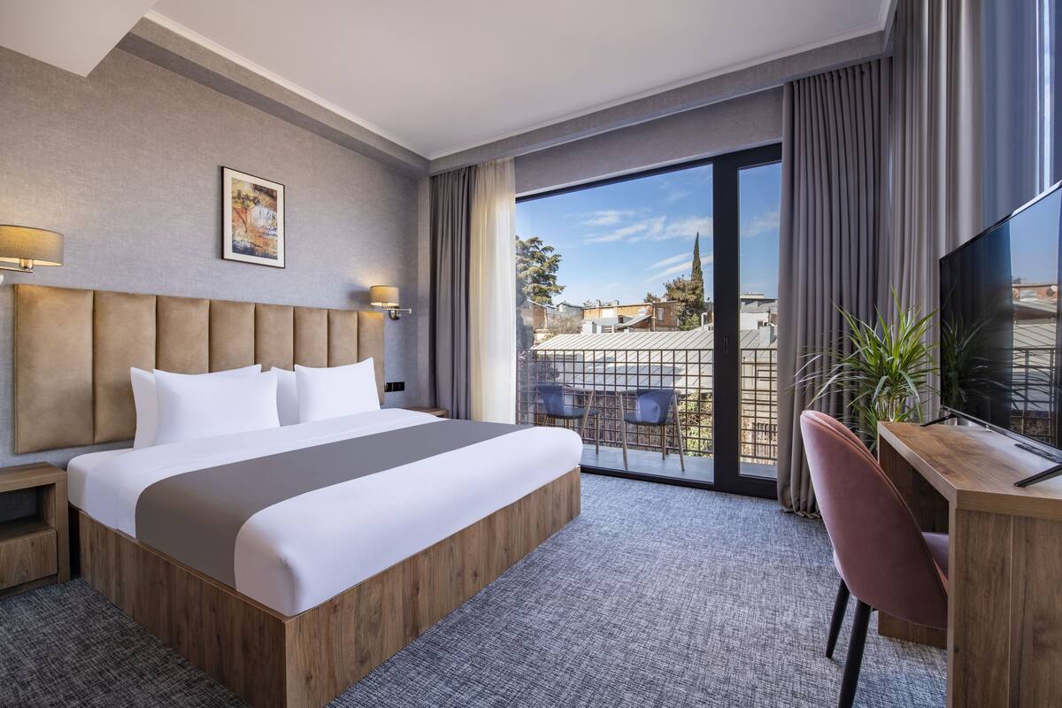 Habitación de hotel moderna con una cama grande, un escritorio y un balcón con vistas.