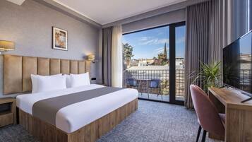 A modern hotel room with a large bed, a desk, and a balcony with a view.