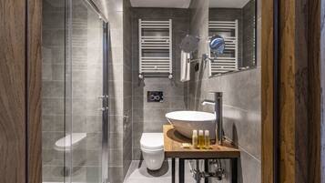 A modern bathroom with a glass shower enclosure, a white toilet, and a wooden vanity with a large sink.