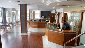 A hotel reception area with a wooden reception desk, a glass display case, and a staircase leading to an upper level. - Hotel J. Balmes Vic (Vic)