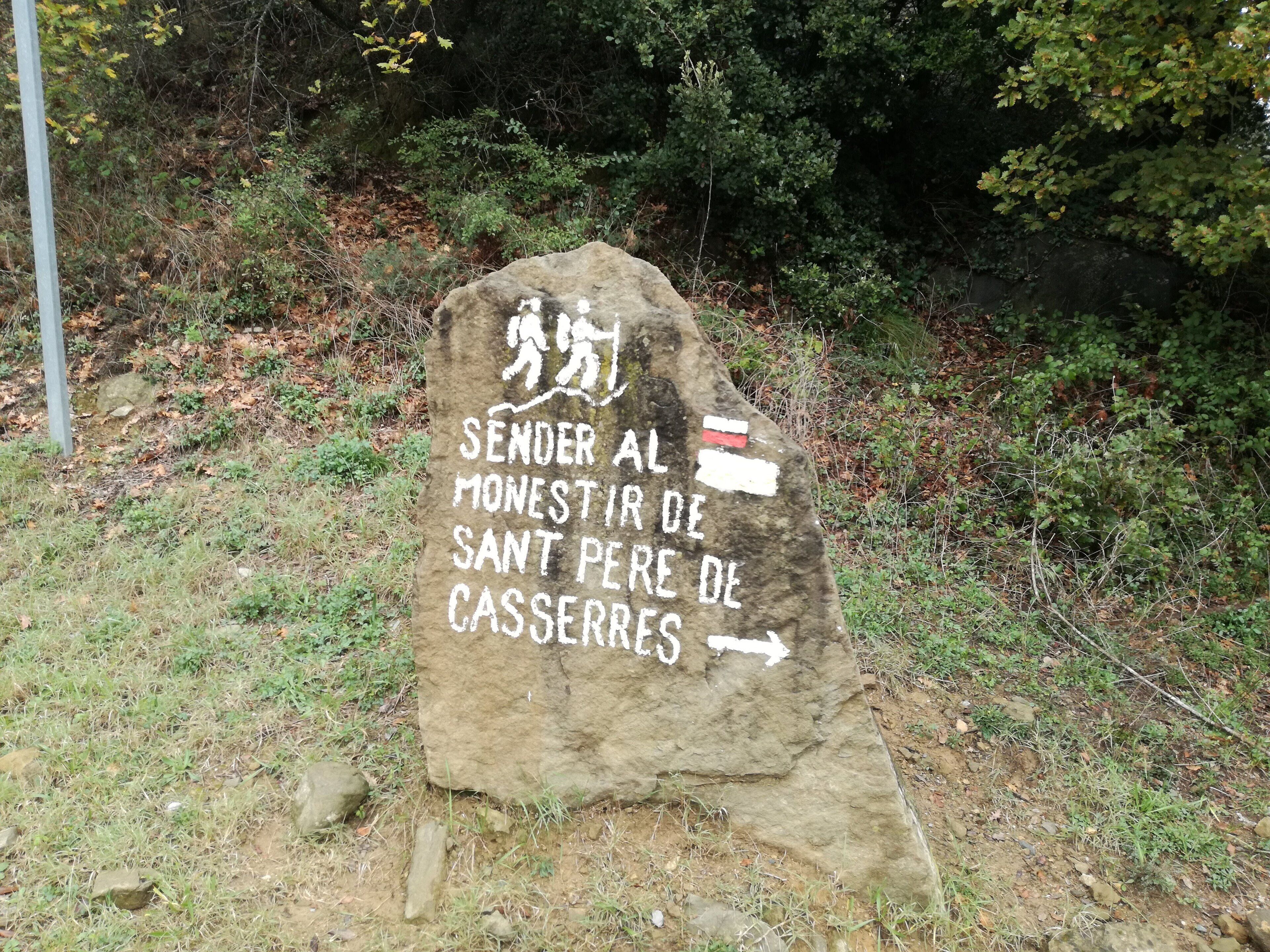 Un cartel de piedra con texto en varios idiomas, rodeado de follaje natural.