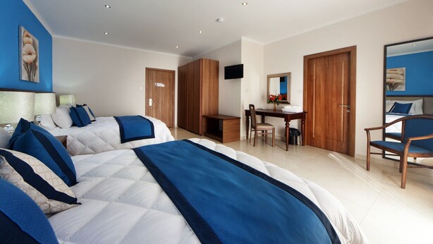Ein Hotelzimmer mit zwei Betten, einem Schreibtisch, einem Sessel und einem Fernseher.