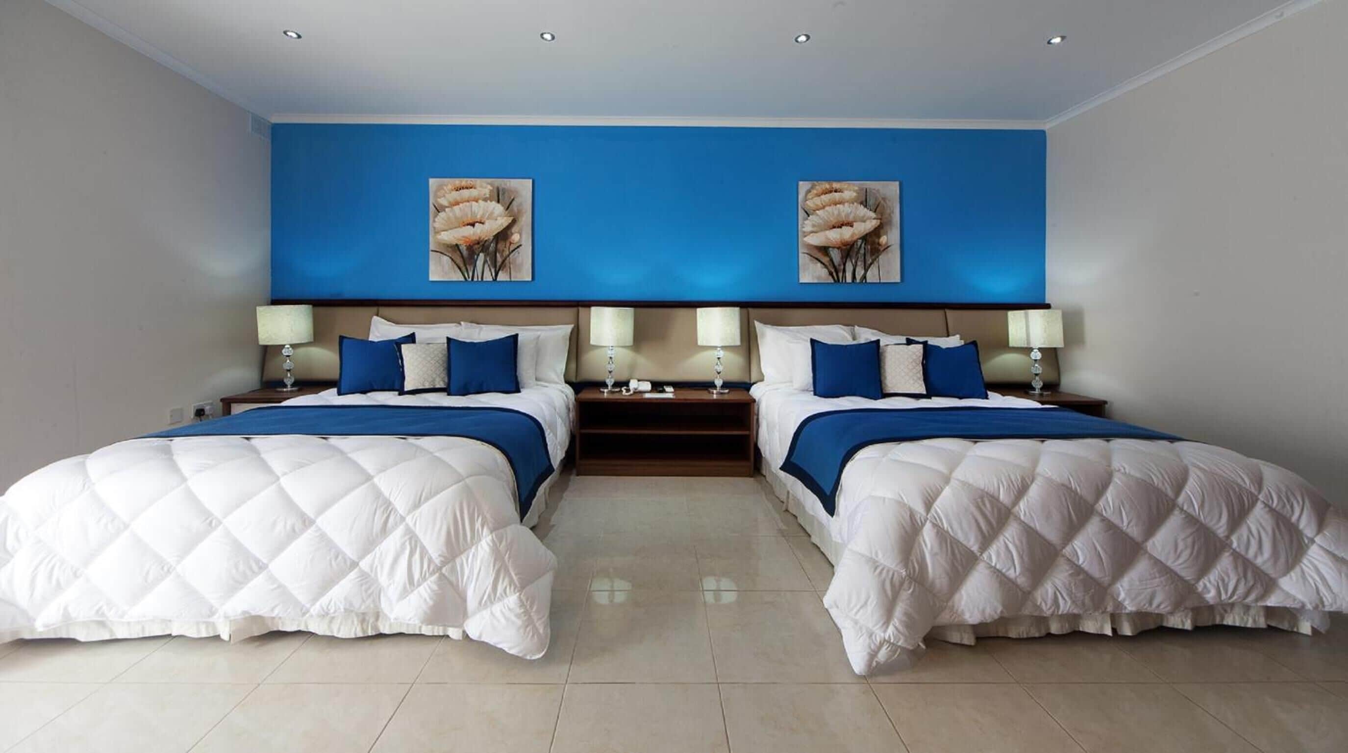 A double room with two beds, a blue accent wall, and artwork above the beds.