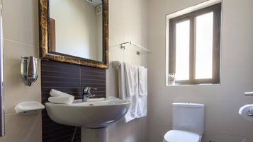 A bathroom with a pedestal sink, a toilet, a window, and a mirror with a decorative frame.