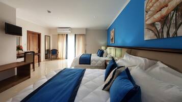 Habitación de hotel con dos camas, un escritorio, una silla, un televisor y un ventanal con cortinas.