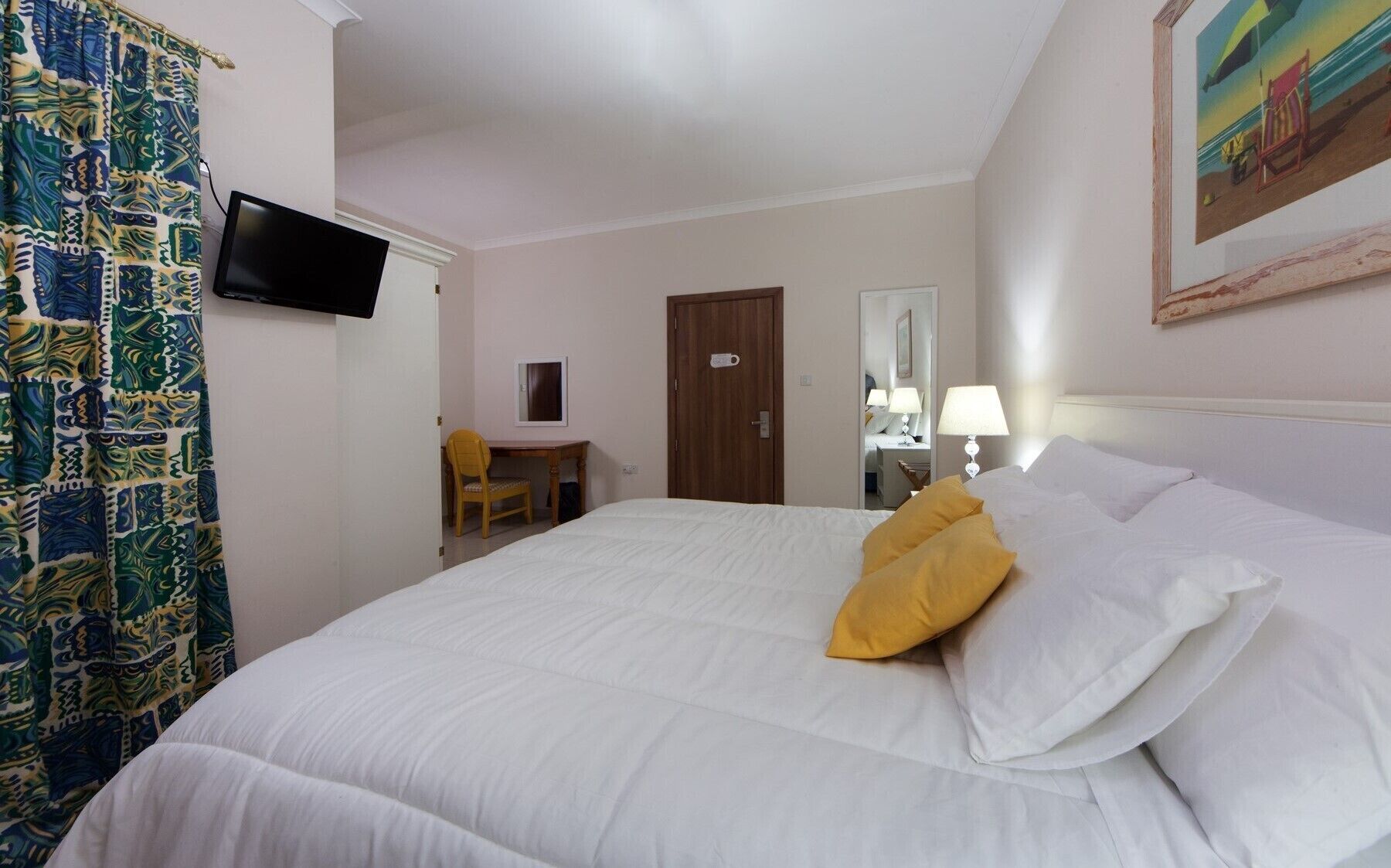 A hotel room with a bed, a desk, a chair, a television, and a painting on the wall.