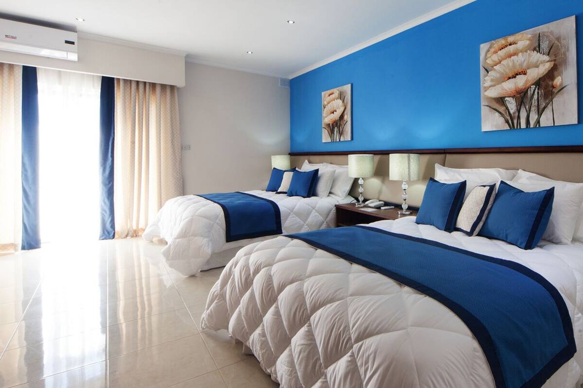 Habitación de hotel con dos camas, un ventanal con cortinas y obras de arte en las paredes.