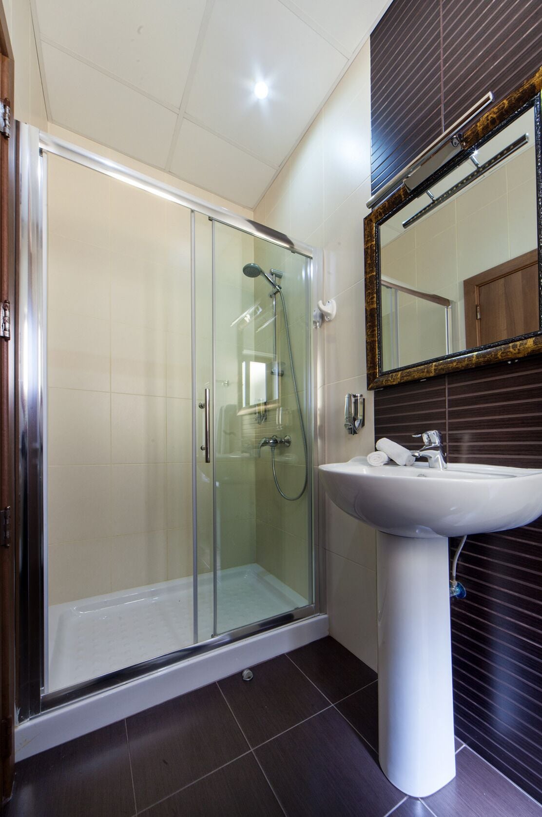 Een moderne badkamer met een douchecabine van glas, een witte wastafel en een grote spiegel met decoratieve lijst.