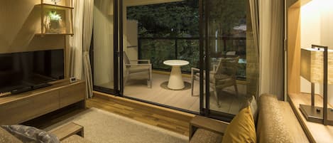 A modern living room with a flat-screen TV, a sofa, a coffee table, and a balcony with a table and chairs.