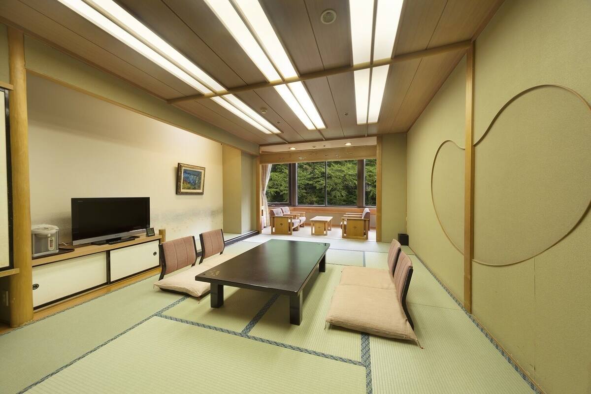 A tatami mat room with a tatami mat table, a television, and a view of the outdoors.