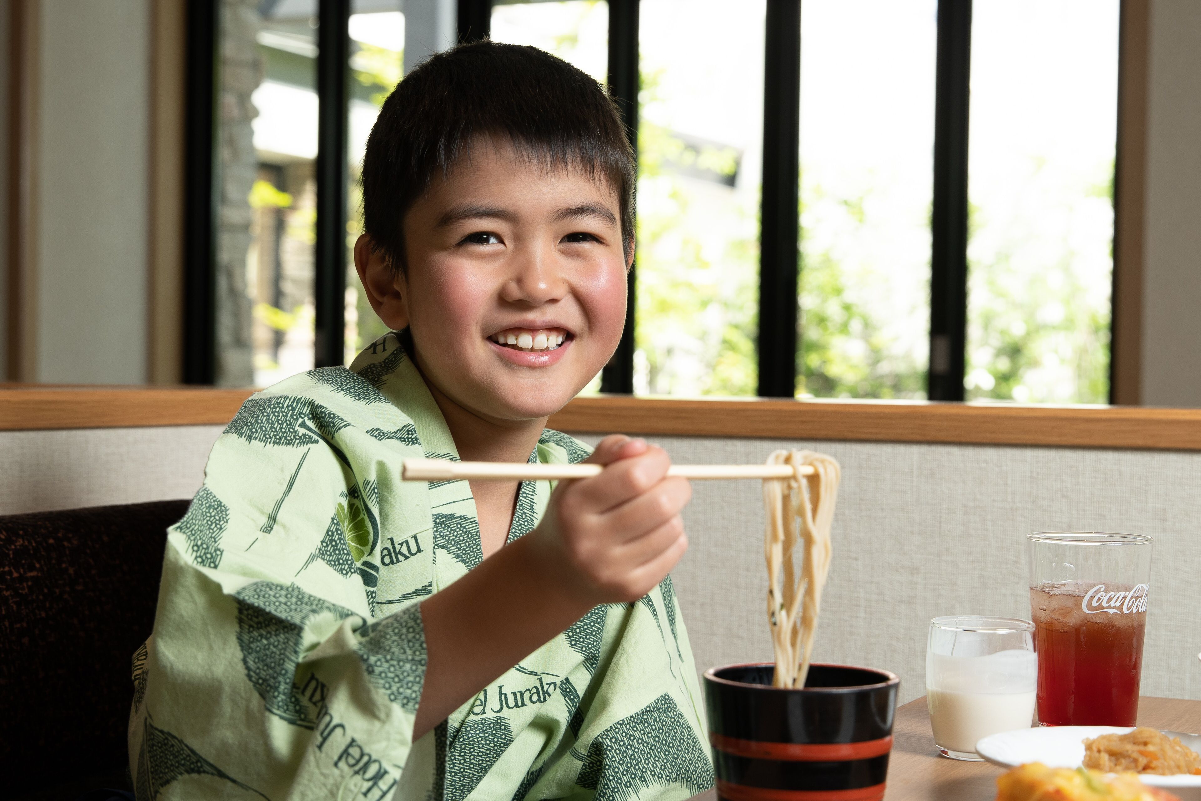 A person sitting at a table with chopsticks, a glass of Coca-Cola, and a cup of milk.