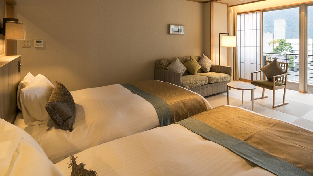 Habitación de hotel con dos camas, un sofá, una mesita y vistas al exterior.
