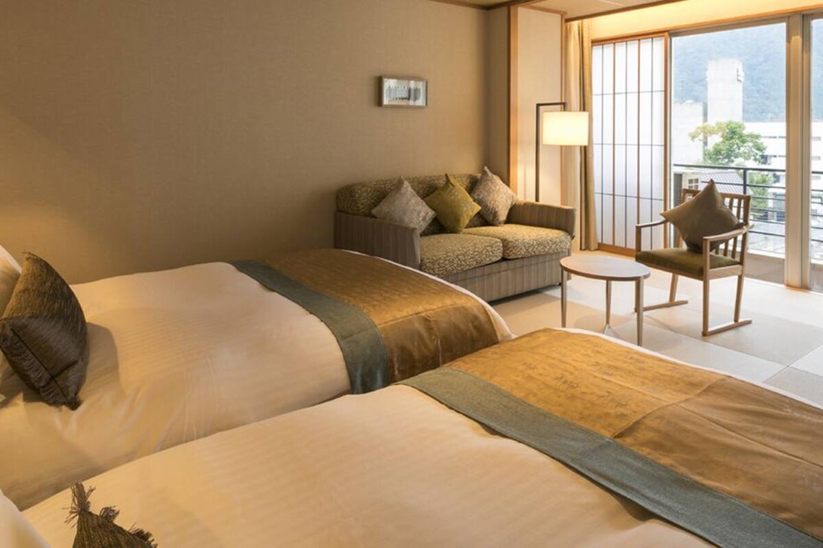 A hotel room with two beds, a sofa, a small table, and a view of the outside.