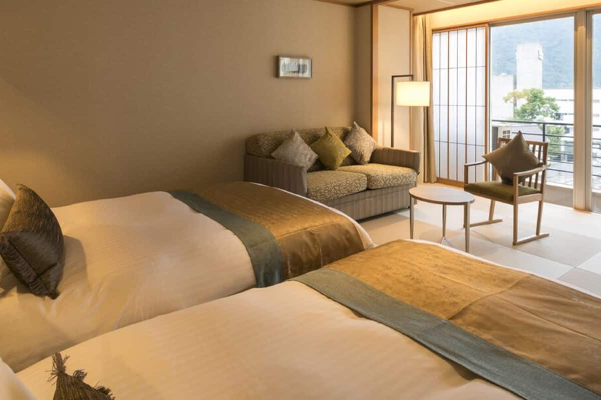 A hotel room with two beds, a sofa, a small table, and a view of the outside.