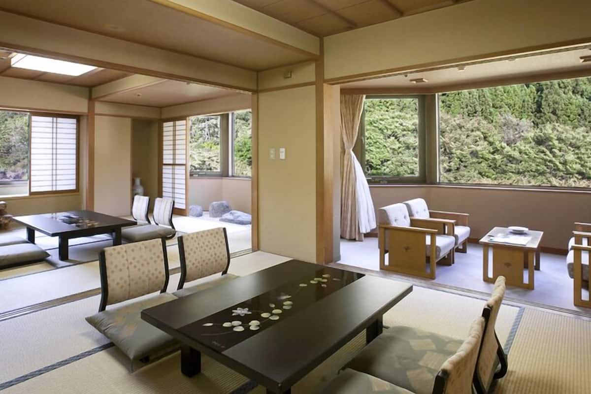 A traditional Japanese room with tatami flooring, a low table with tea set, and a view of greenery outside.