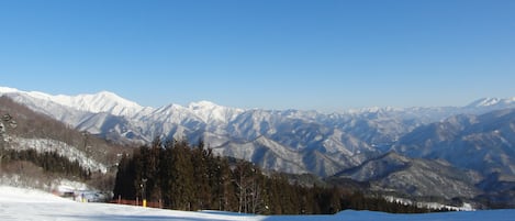 Un paisaje nevado con tres personas sentadas en un trineo, un cielo azul despejado y montañas cubiertas de nieve al fondo.