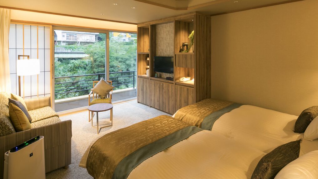 Habitación de hotel con una cama grande, un sofá, una mesita y un televisor sobre una estantería de madera.