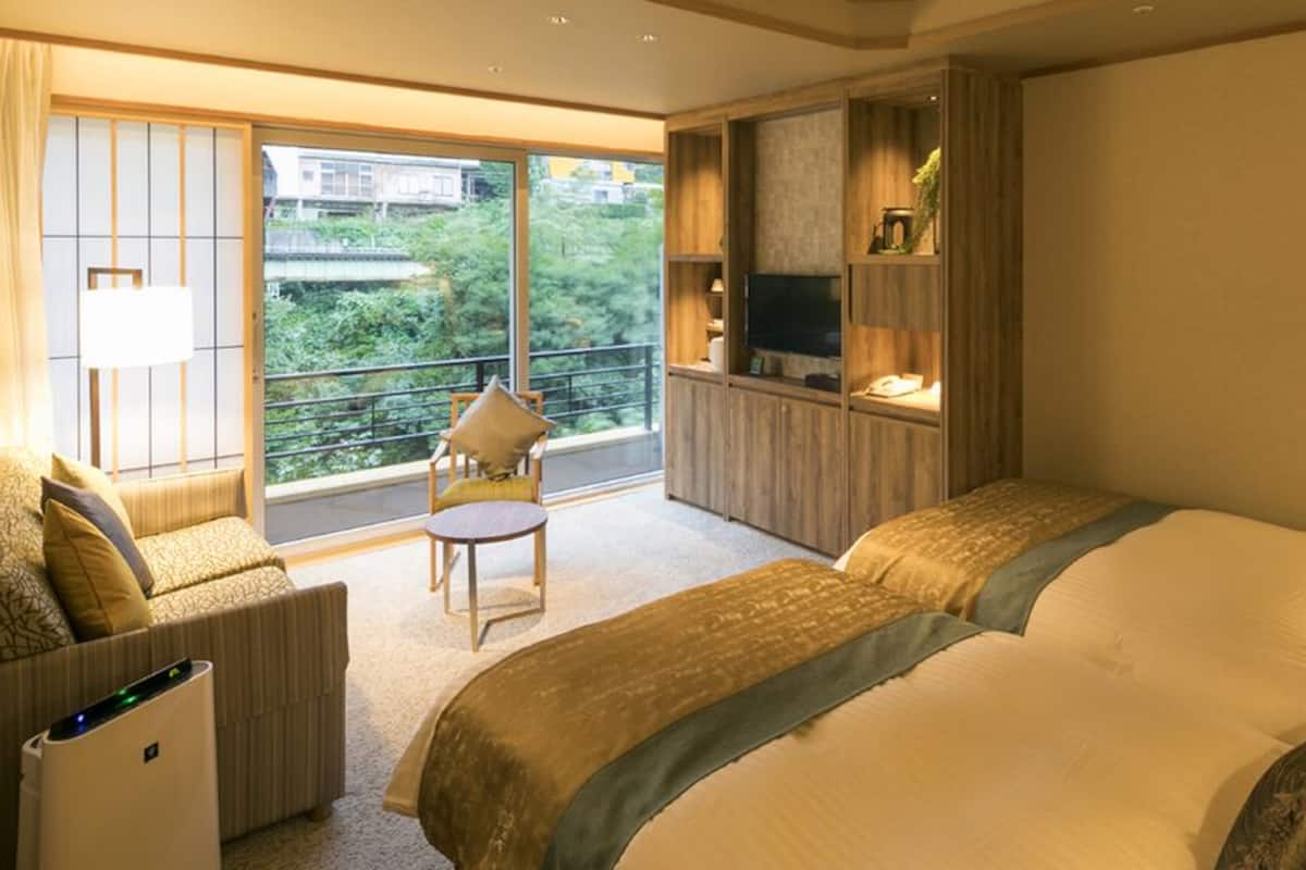 A hotel room with a large bed, a sofa, a small table, and a TV on a wooden shelf.
