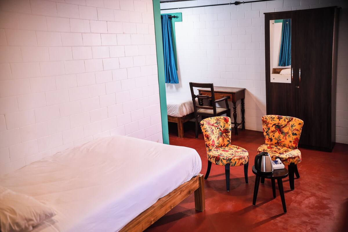 A room with a single bed, two floral-patterned chairs, a wooden desk, and a dark door.